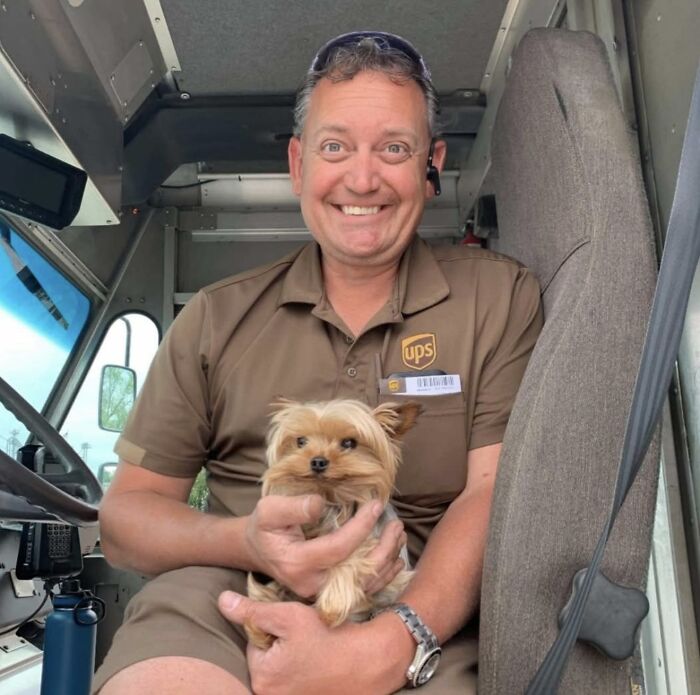UPS driver smiling inside delivery truck holding a small adorable pet dog, showcasing pet encounters.