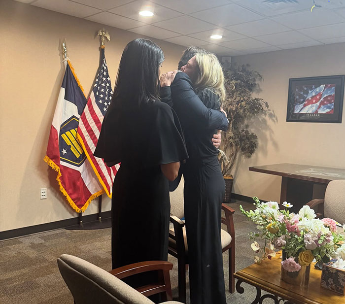 Two women embracing in an office with American flags, symbolizing FBI revealing chilling note and DNA evidence links.