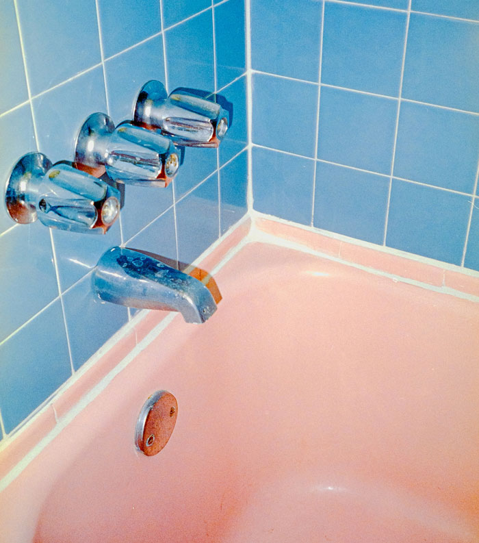 Vintage pink bathtub with blue tiled wall and silver faucets, evoking creepy things that happened while home alone.