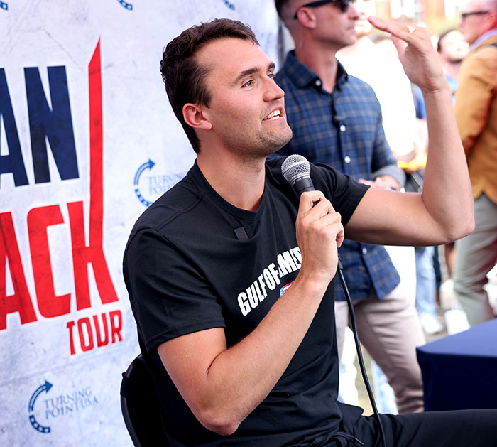 Man speaking into microphone at an event, discussing the Jimmy Fallon and Jimmy Kimmel show suspension topic.