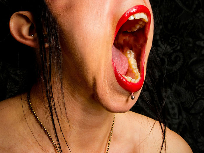 Close-up of person with bright red lipstick, mouth wide open, showing teeth and tongue, illustrating professors with hilarious reviews.