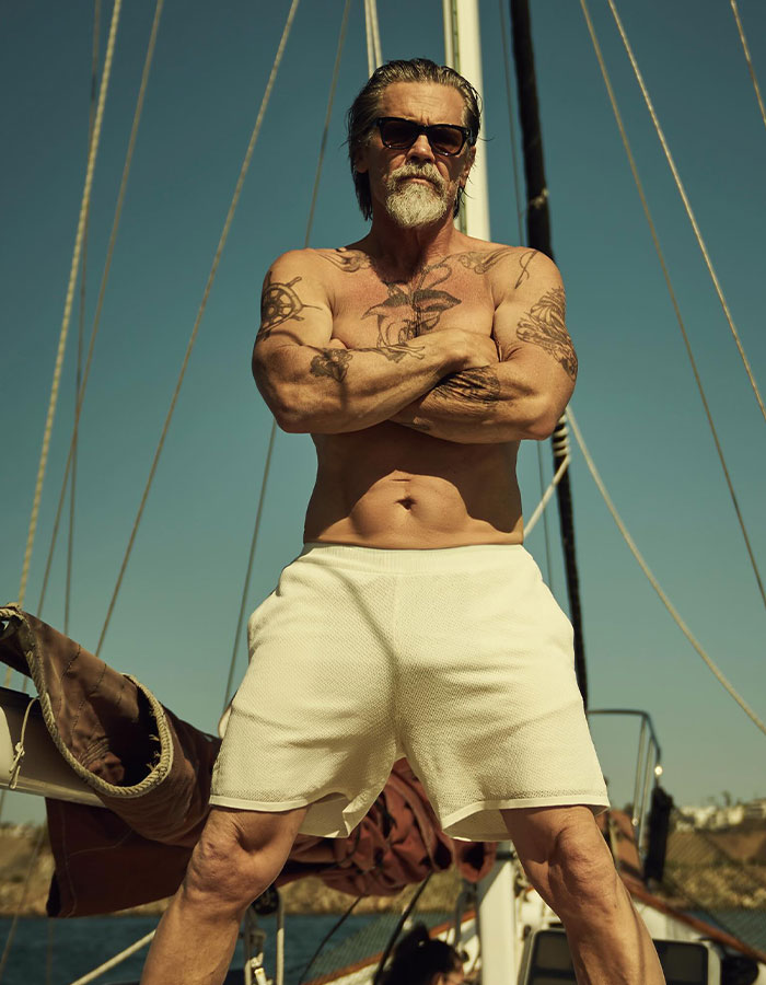 Shirtless tattooed man wearing sunglasses stands confidently on a boat under clear sky, representing celeb confessions memoirs.