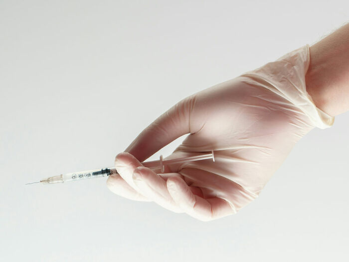 Hand wearing medical glove holding syringe, representing Kybella treatment for facial fat reduction and transformation. Hand wearing medical glove holding syringe, representing Kybella treatment for facial fat reduction and transformation.