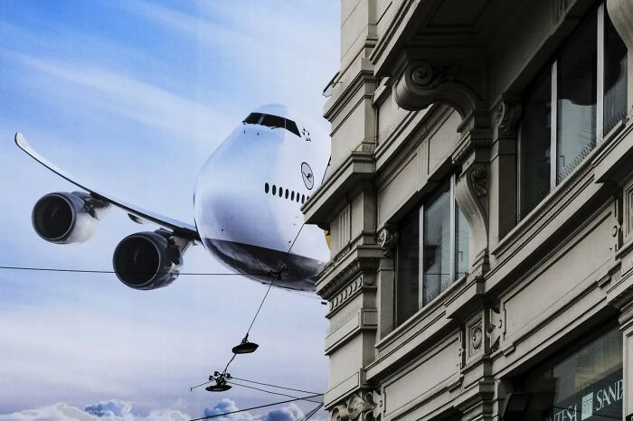 Street photo showing a plane seemingly hanging from a building, a funny coincidence in urban photography.