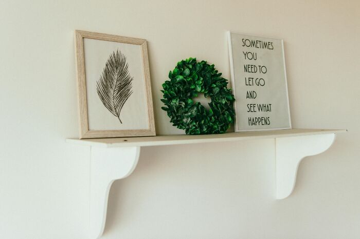 Minimalist shelf with framed leaf art, green wreath, and motivational sign highlighting everyday adulting skills.