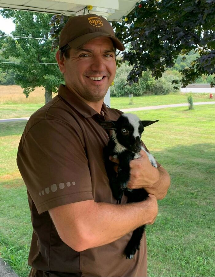 UPS driver smiling and holding an adorable black and white baby goat outdoors in a green grassy area