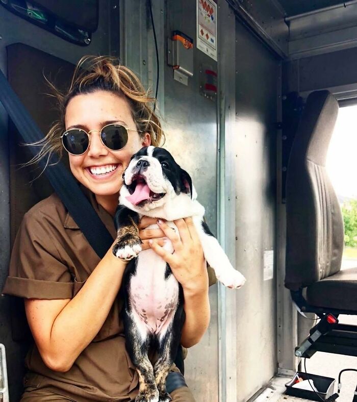 UPS driver holding an adorable puppy inside a delivery truck, smiling and enjoying a moment with a cute pet.