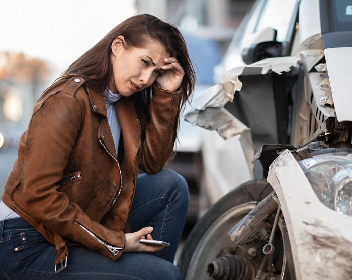 Woman in brown jacket looking distressed after a car accident, highlighting life-changing moments folks tattooed on their hearts.
