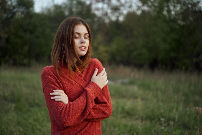 Young woman in red sweater standing outside with eyes closed, reflecting on life-changing sentences tattooed on hearts.