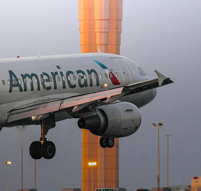 American Airlines airplane landing near airport tower, illustrating flight attendant and big breasts discrimination issues.