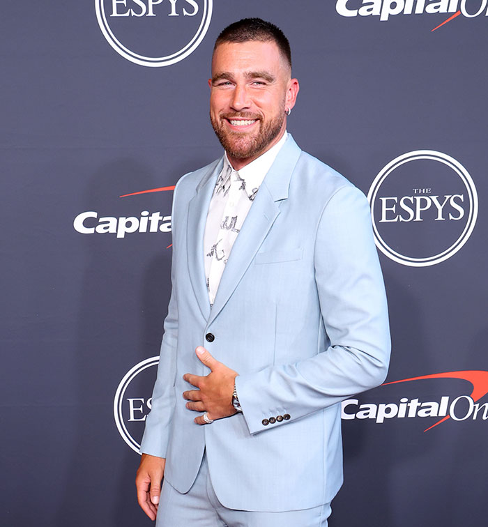 Travis Kelce in a light blue suit smiling on the red carpet, related to his answer about Taylor Swift in a viral video.