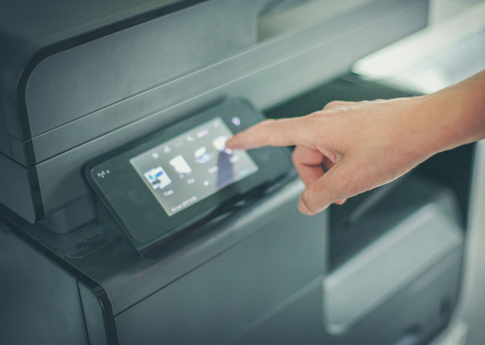Person’s hand interacting with touchscreen display on a modern office printer showing digital menu options.