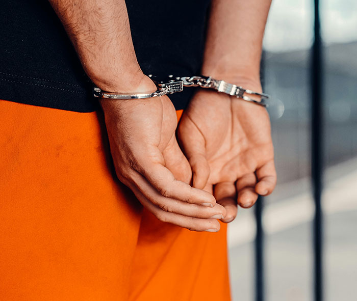 Close-up of a person in handcuffs wearing an orange uniform, symbolizing a teacher arrested at school for causing damage and sickness.