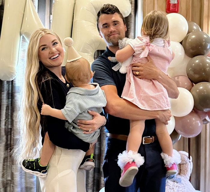 Family portrait with parents holding two children at a party, unrelated to sisters who destroyed Charlie Kirk memorial or homelessness.