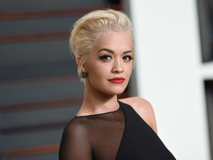 Blonde celeb with bold red lipstick and winged eyeliner in a black sheer dress at a formal event, representing cringey celeb moments.