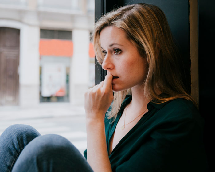Woman sitting by window looking thoughtful and worried, reflecting on giving husband another chance and lessons learned.