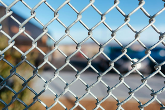 Chain-link fence close-up with blurred parking lot background representing security guards on the job sharing creepy experiences