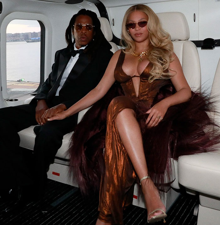 Ashley Graham in a body-hugging dress showcasing her figure, seated inside a luxury vehicle with a companion.