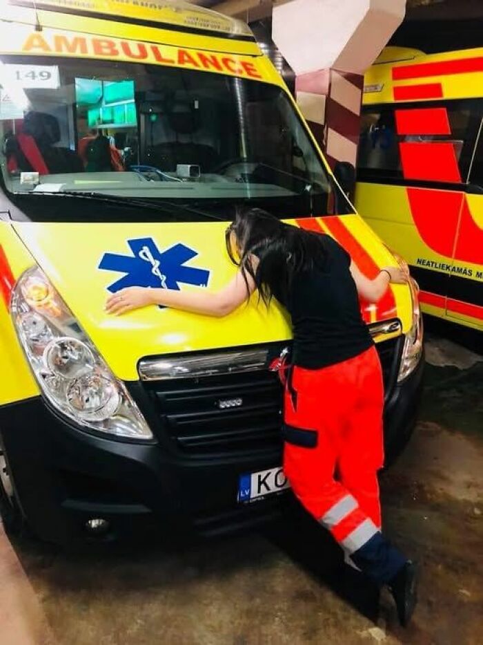 Paramedic in red pants leaning on a yellow ambulance, showing exhaustion after a long shift in an emergency medical setting.