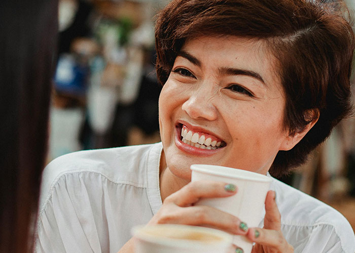 Woman smiling while holding a cup during a casual conversation, illustrating men’s views on creepy behavior crossing the line.