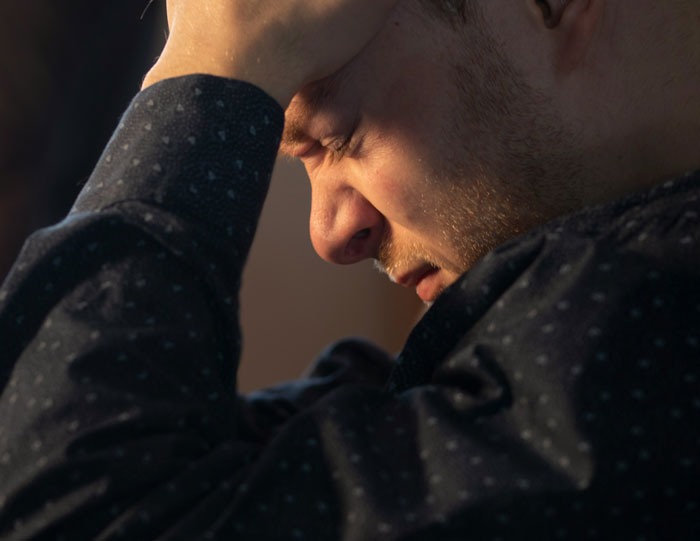 Man in dark shirt holding head in distress, illustrating creepy things that happened while home alone experience.
