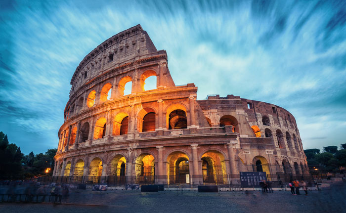 Ancient Roman Colosseum illuminated at dusk with tourists nearby, symbolizing professors who left lasting impressions on students.