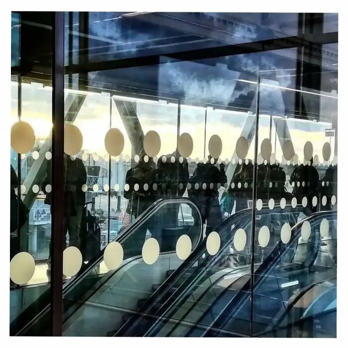 Reflection showing people and escalator with dots aligning perfectly, a funny coincidence in street photos.