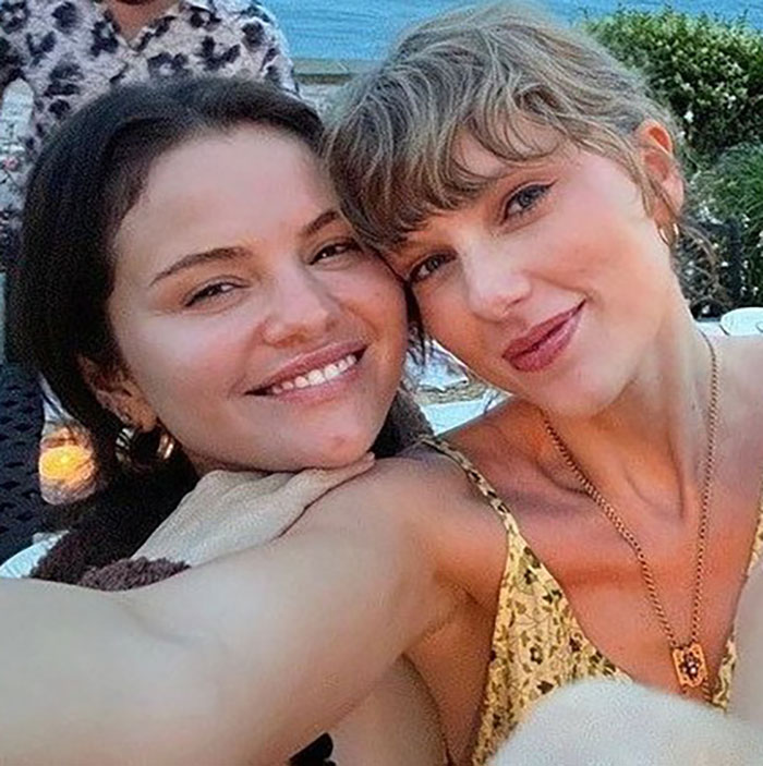 Taylor Swift and Selena Gomez smiling closely together at an outdoor wedding, capturing a joyful best friend moment.