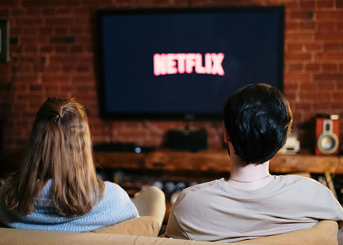 Two people sitting on a couch watching Netflix on TV, illustrating common purchases ditched due to high price tags.