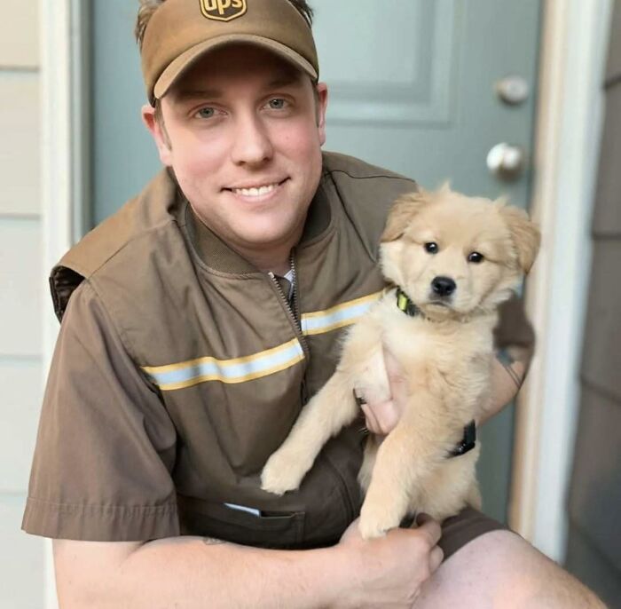 UPS driver smiling and holding an adorable fluffy puppy outside a home, showcasing a heartwarming pet moment.