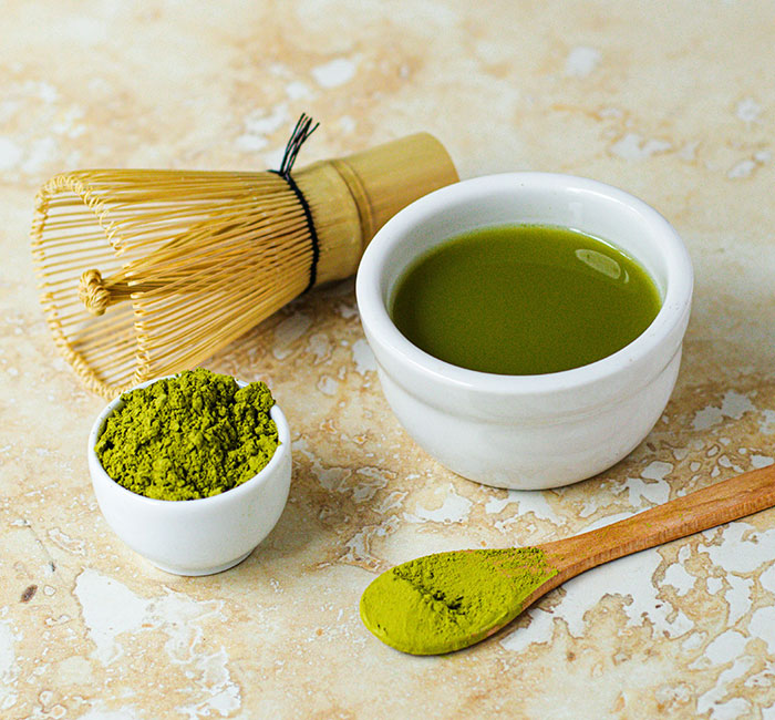 Matcha powder and drink in a white bowl with a bamboo whisk and spoon on a marble surface, health warning concept.