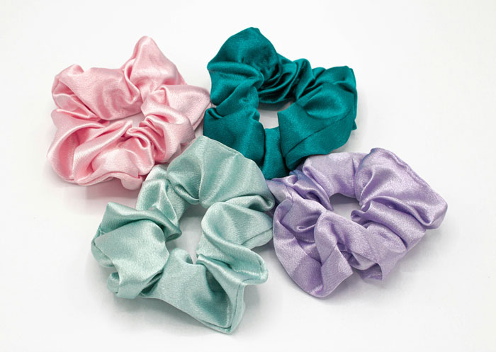 Four colorful satin scrunchies in pink, teal, mint, and lavender, highlighting unexpected things about women accessories.