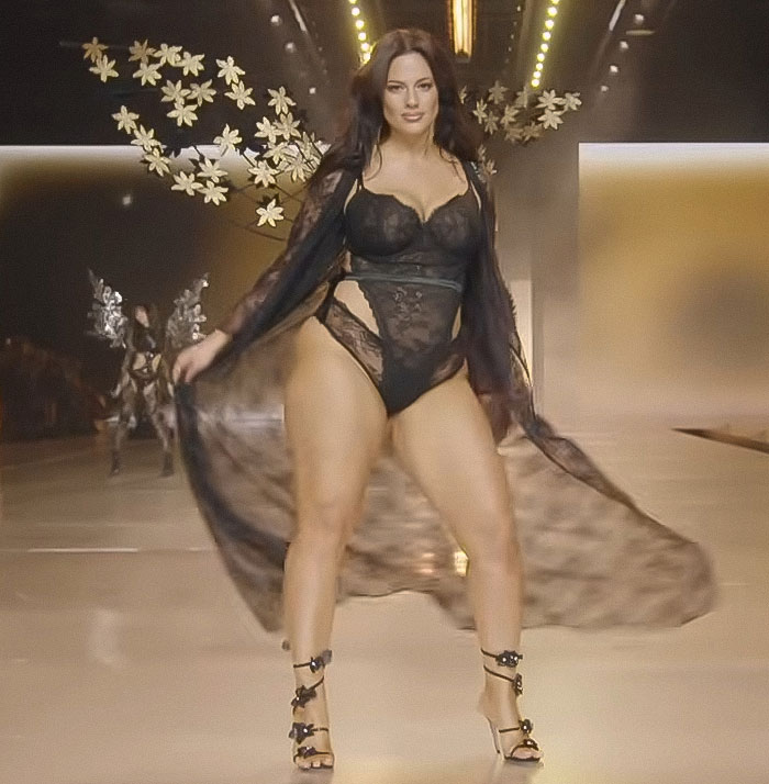 Ashley Graham on runway wearing a body-hugging dress highlighting her figure with sheer black lace details.