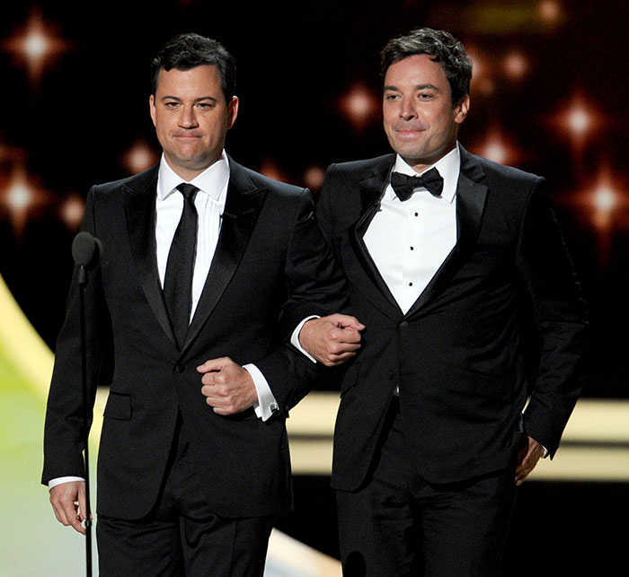 Jimmy Fallon and Jimmy Kimmel in black tuxedos appearing on stage together at a formal event, highlighting show suspension talks.