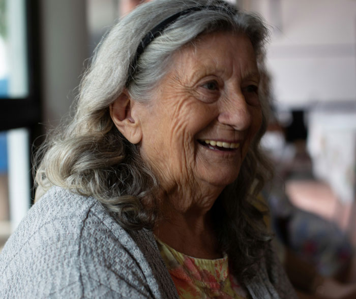 Smiling elderly professor with gray hair and headband, creating a memorable impression on students in a cozy indoor setting