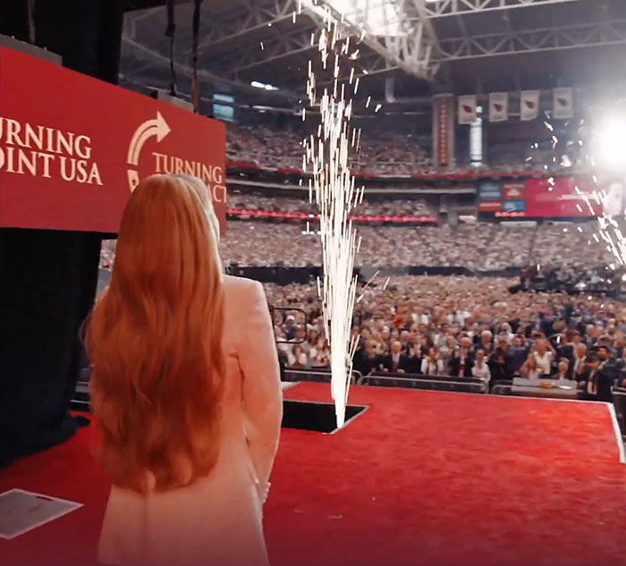 Woman with long red hair on stage with fireworks and a large crowd, capturing WWE level stuff surprising entrance. Woman with long red hair on stage with fireworks and a large crowd, capturing WWE level stuff surprising entrance.