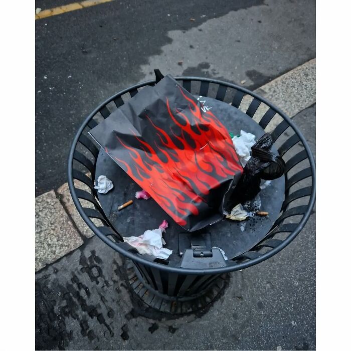 Trash can with a flame-patterned bag inside, creating a funny street photo coincidence in an urban setting.
