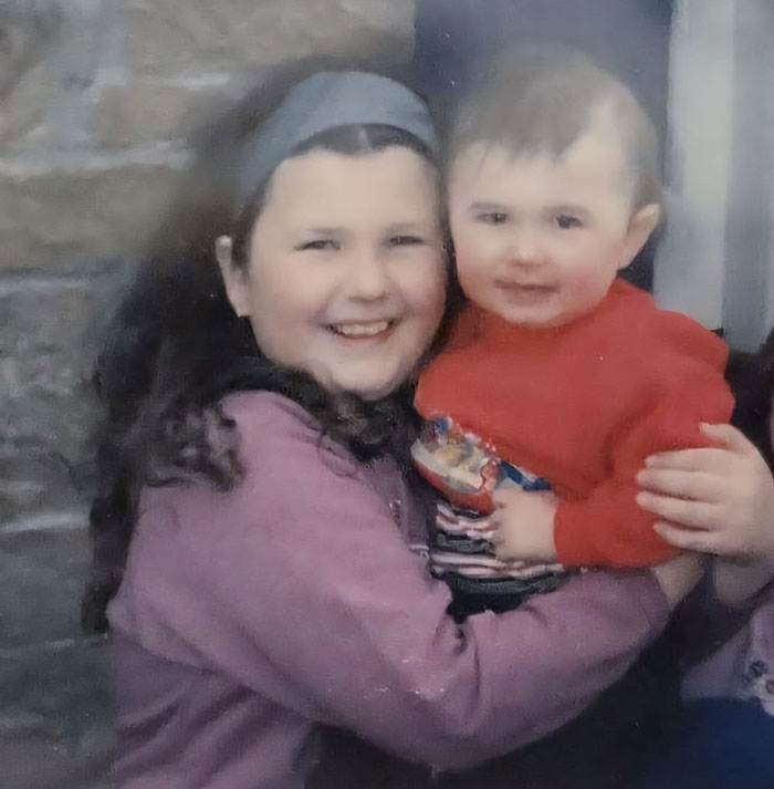 Young girl smiling and holding a toddler in a red sweater, related to American Nightmare mom who married man she met online.