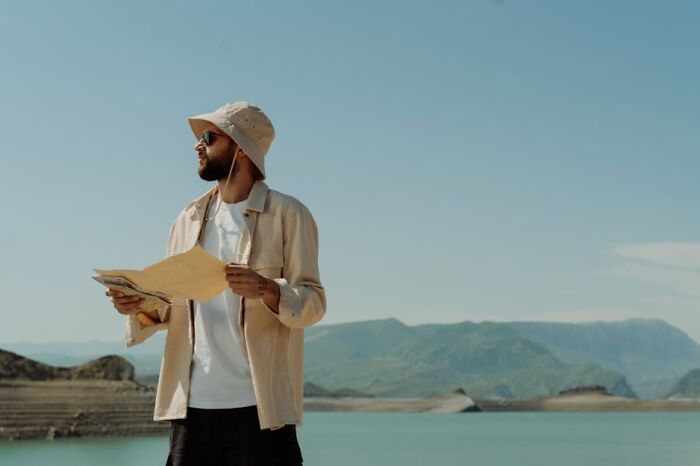 Man wearing a hat holding a map by the lake, showing confidence in adulting and everyday skills outdoors.