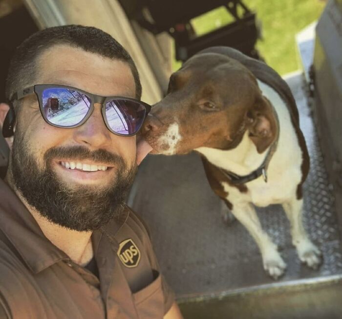 UPS driver in uniform smiling as an adorable dog licks his cheek during a friendly pet encounter on delivery route