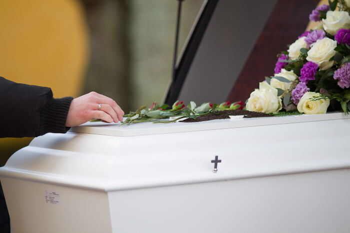Person placing flowers on a white coffin with a cross, symbolizing life-changing sentences tattooed on their hearts.