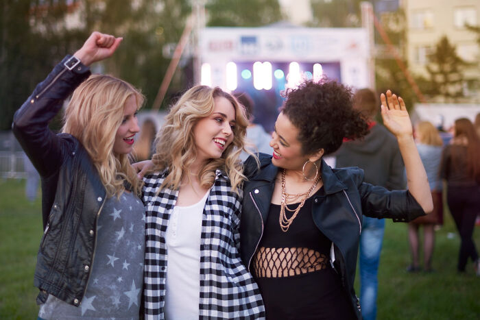 Three friends enjoying an outdoor concert, captured while sharing happy moments during online surfing discoveries.