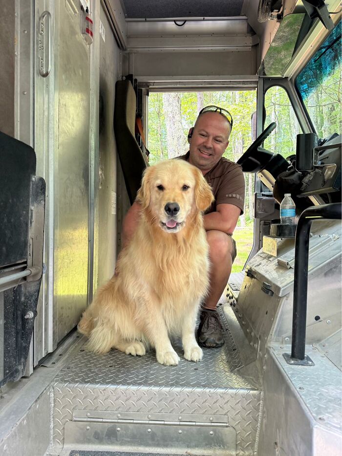 UPS driver sitting inside delivery truck with a golden retriever, showcasing adorable pets met during deliveries.