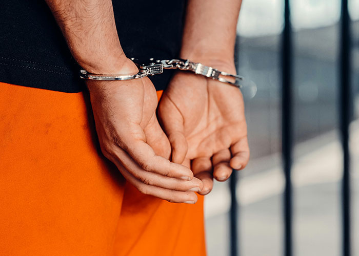 Person wearing orange pants with hands cuffed behind back, illustrating criminal fails in a detention setting.