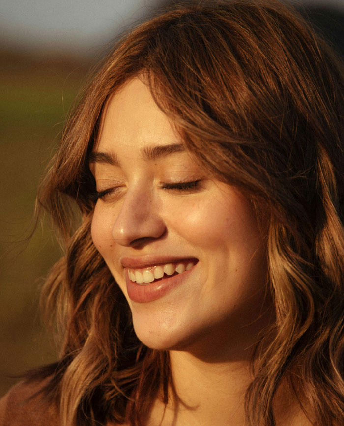 Young woman with eyes closed smiling peacefully outdoors, illustrating the benefits of sleep for mental well-being and problem-solving.