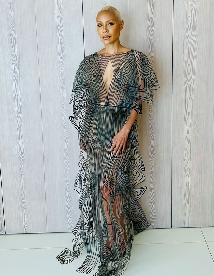 Woman in a sheer black patterned dress posing against wood panel wall, representing raw and unfiltered confessions celebs shared.