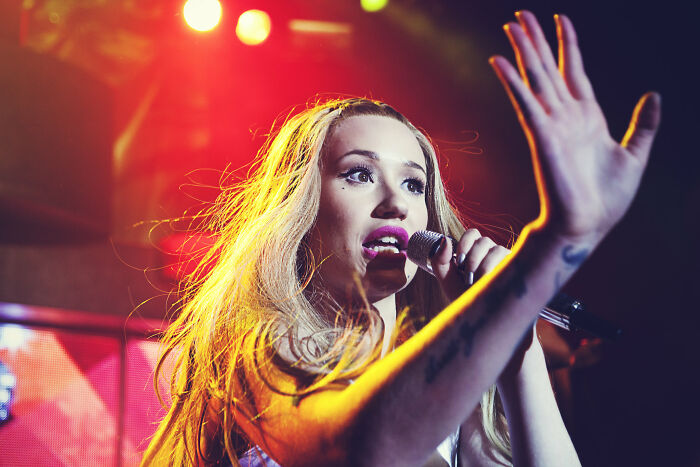 Female singer with long blonde hair holding a microphone, performing on stage under bright colorful lights about nasty ex behavior.