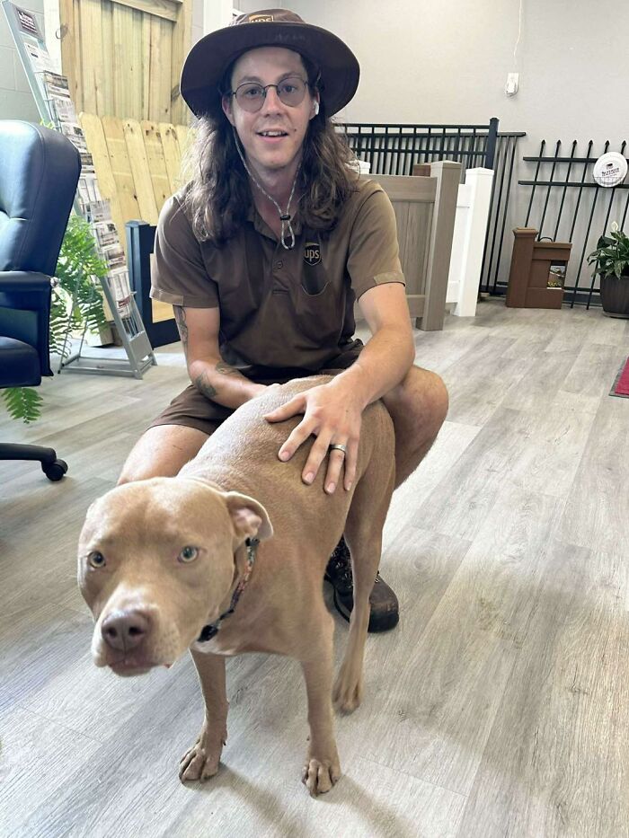 UPS driver kneeling indoors, smiling and petting a light brown dog, showcasing a friendly moment with adorable pets.