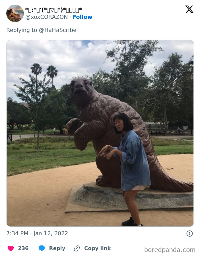Person mimicking pose of large animal statue in a park, illustrating life imitating art with playful interaction outdoors.