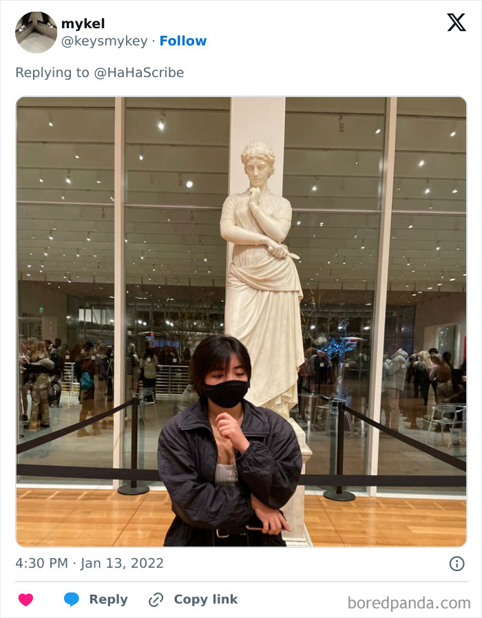 Person mimicking statue pose in museum, illustrating life imitating art with a thoughtful expression and black face mask.
